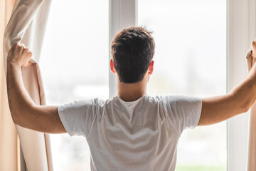 Photo of middle aged man opening curtains in hotel room in the morning.