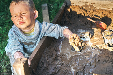 Funny dirty boy playing with toy cars in the sandbox