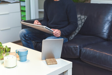 Man working at home from desk in a living room with tablet and note pad