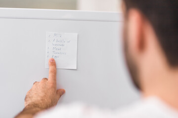 Handwritten shopping list with ballpoint pen pinned on white fridge.