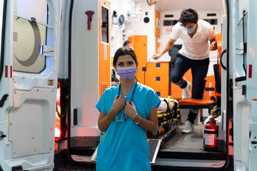 Portrait of young female paramedic with face mask working in an ambulance during pandemic