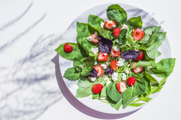 Summer vegetables salad with fresh strawberries, basil, mozzarella on white background in garden at sunny day. The concept of proper nutrition and healthy eating. Organic and vegetarian food.