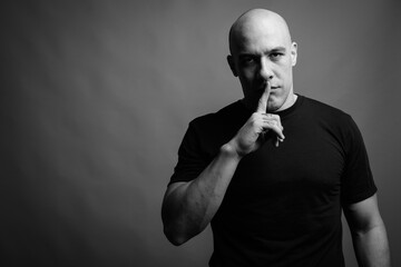 Handsome bald man against gray background in black and white