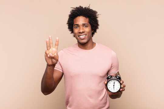 young black afro man smiling and looking friendly, showing number three or third with hand forward, counting down