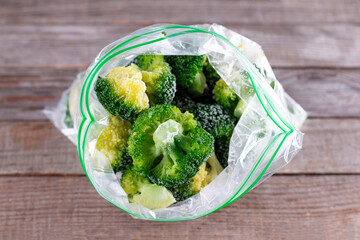 Frozen broccoli in a plastic bag on wooden table. Selective focus.
