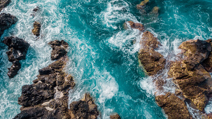 Stones among turquoise waves and sea foam from above. Atlantic ocean coastline with rocks. Madeira...