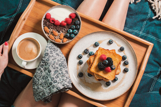 Cozy Breakfast In Bed. Woman Legs. Yogurt Bowl With Raspberries, Blueberry, Chocolate And Nuts, French Toasts, Coffee Cup On Wooden Plate. Close Up Still Life From Above. Food Photography. 