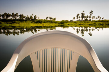Close-up of an empty white plastic stackable chair with arms, and in the background the lush Coyuca...