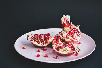 Juicy pomegranate on a pink plate and black background.