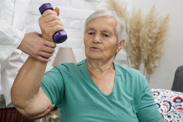 Therapist assisting senior woman with exercises. Elderly patient using dumbbells in the physical therapy session. Rehabilitation health care concept.