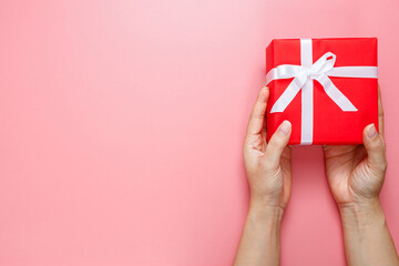Flat lay of woman hands holding gift wrapped and decorated with bow isolated on pink background.