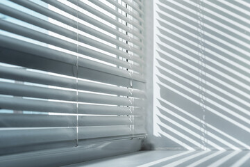 sun lighting throuhg white open shutter and falling gray shadow on wall and window sill