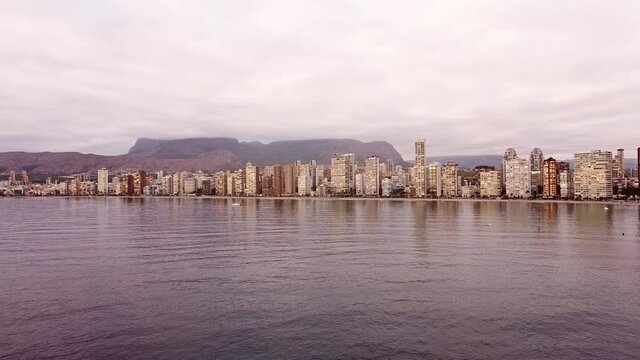 Aerial view of a cloudy seaside city. Daytime skyline of Benidorm, Spain. Pan shot. Slow motion.