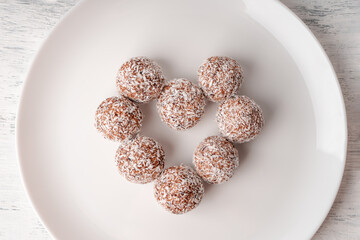 White plate with round sweets made of dates and coconut shavings laid out in the shape of a heart top view
