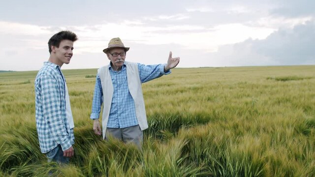 Happy senior farmer admiring of good barley harvest and embracing son in field