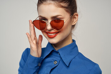 Fashionable woman in sunglasses and a blue shirt gesturing with her hands on a light background cropped view