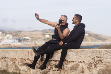 two divers sitting on a fence taking a selfie