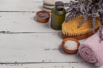 The concept of SPA. Flat layer of dry lavender flowers, essential oil, sea salt, flat stones, scented candle, pink bath towel on a wooden white background.