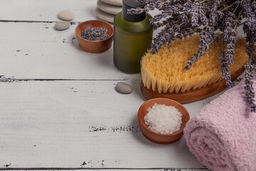 The concept of SPA. Flat layer of dry lavender flowers, essential oil, sea salt, flat stones, scented candle, pink bath towel on a wooden white background.