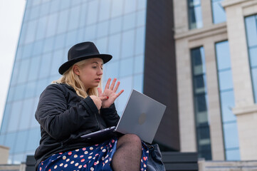 Young woman speaks sign language on a video call on a laptop outdoors. The deaf-mute girl...