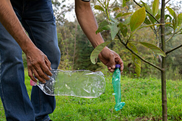 Fototapeta premium hands of a man picking up a plastic bottle in a forest for recycling