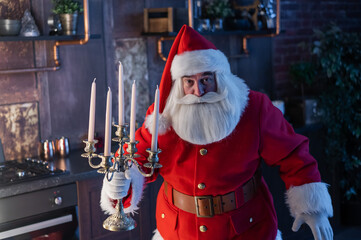 Santa claus sneaks up at night and holding a candelabrum. - obrazy, fototapety, plakaty