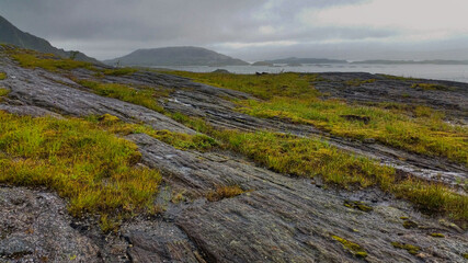 Fototapeta na wymiar View to hiking trail to Dønnamannen peak going upwards a grey stone mountain slope covered by grass and moss in the Dønna island 
