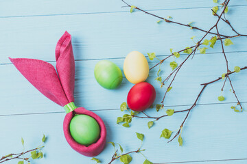 Easter eggs and the shape of rabbit ears and tree branches with green leaves, on a blue wooden background, selective focus, tinted image