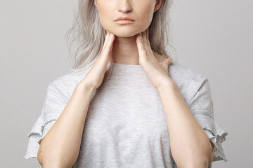 Female checking thyroid gland by herself. Close up of woman in white t- shirt touching neck with...