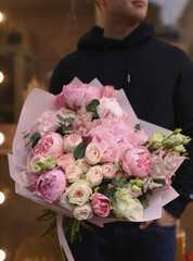 Young man holding big beautiful blossoming bouquet in pink color of fresh flowers wrapped in pink paper.