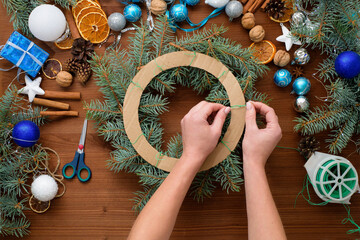 step-by-step process of making a Christmas tree wreath at home from spruce branches, oranges and Christmas balls in the silver and blue colors of the 2021 bull . wooden background top view