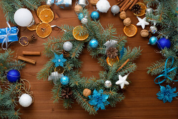 step-by-step process of making a Christmas tree wreath at home from spruce branches, oranges and Christmas balls in the silver and blue colors of the 2021 bull . wooden background top view