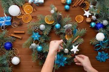 step-by-step process of making a Christmas tree wreath at home from spruce branches, oranges and Christmas balls in the silver and blue colors of the 2021 bull . wooden background top view