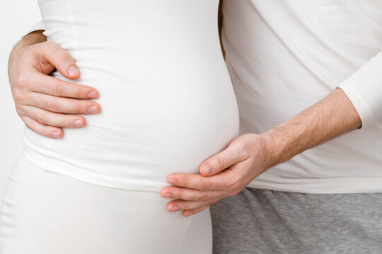 Young man hands hugging and touching pregnant woman belly. Emotional loving pregnancy time - 20 weeks. Baby expectation. Happiness and safety concept. Front side view. Closeup.