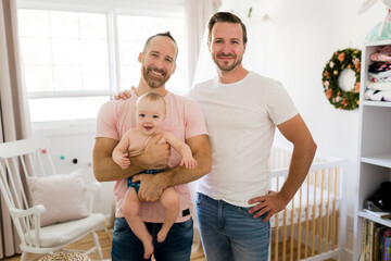 Male gay parents relaxing in baby room holding it - obrazy, fototapety, plakaty