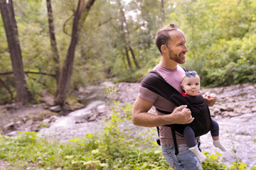 beautiful caring father holding her baby child in a sling walking on nature