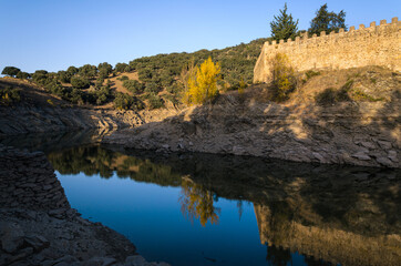 Autumnal landscape with the Lozoya river passing by the walls of Buitrago de Lozoya and the trees with autumn colors, Madrid, Spain