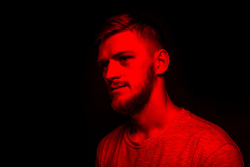 Low key portrait of bearded young man in red light on black backdrop copy space. Warning of global problems, climate warming, threat of extinction of life on earth. Social ads Layout