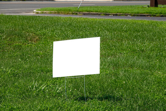 Blank White Lawn Sign On Metal Spikes On Green Grass Near A Sidewalk And Street