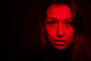 close up Low key full-face portrait of pretty girl looking at camera dilated pupil in creepy red light copy space. Layout for advertising social assistance to domestic violence victims. Hope concept