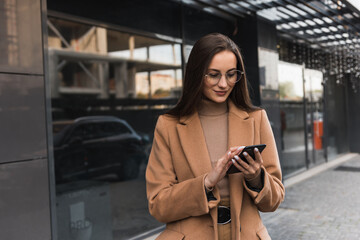 Portrait of a beautiful caucasian businesswoman standing near the office and typing on her cell phone.