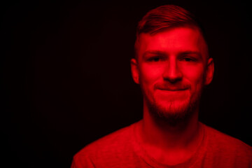 Low key portrait of bearded young confident man full-face looking at camera red light on black backdrop copy space. Layout for ads social assistance, call line for singles. Stress management concept