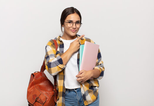 young hispanic woman smiling cheerfully, feeling happy and pointing to the side and upwards, showing object in copy space