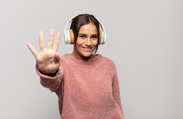 young hispanic woman smiling and looking friendly, showing number four or fourth with hand forward,...
