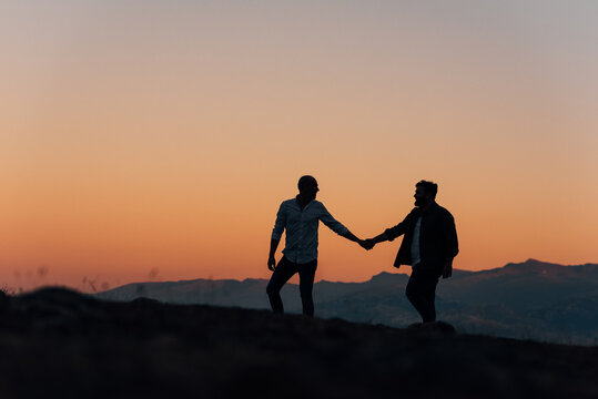 Silhouette of a gay couple holding hands walking at sunset.
