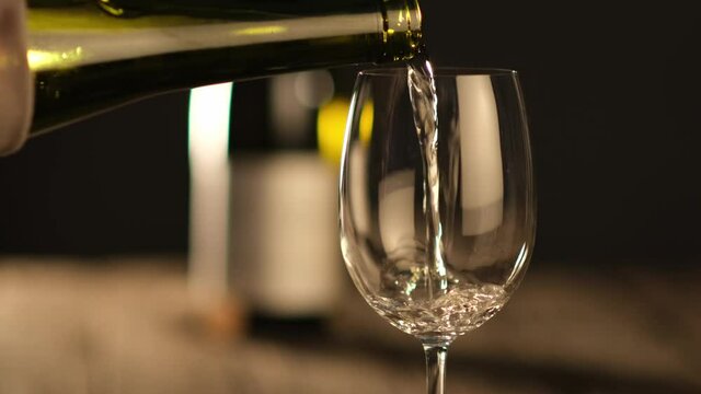 waiter pouring white wine in a glass on a wooden restaurant table