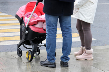 Fototapeta premium Couple with a kid in baby stroller standing in front of pedestrian crossing. Concept of road safety, parents with child in autumn city