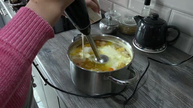 woman prepares pumpkin soup in a saucepan. pour the cream into a saucepan where the pumpkin is already boiled and turn on the blender