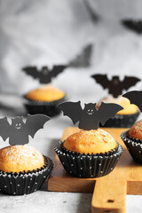 Halloween pumpkin muffins in black capsules decorated with cardboard bats. Festive Halloween cupcakes. Close-up view of delicious spooky halloween muffins on the grey table. Halloween recipes