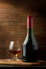 Bottle and glass of brandy on a wooden background.